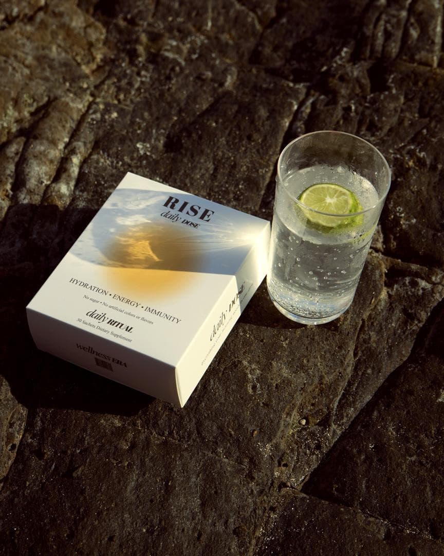 A box of RISE Daily Dose on dark stone next to a glass of sparkling water with lime