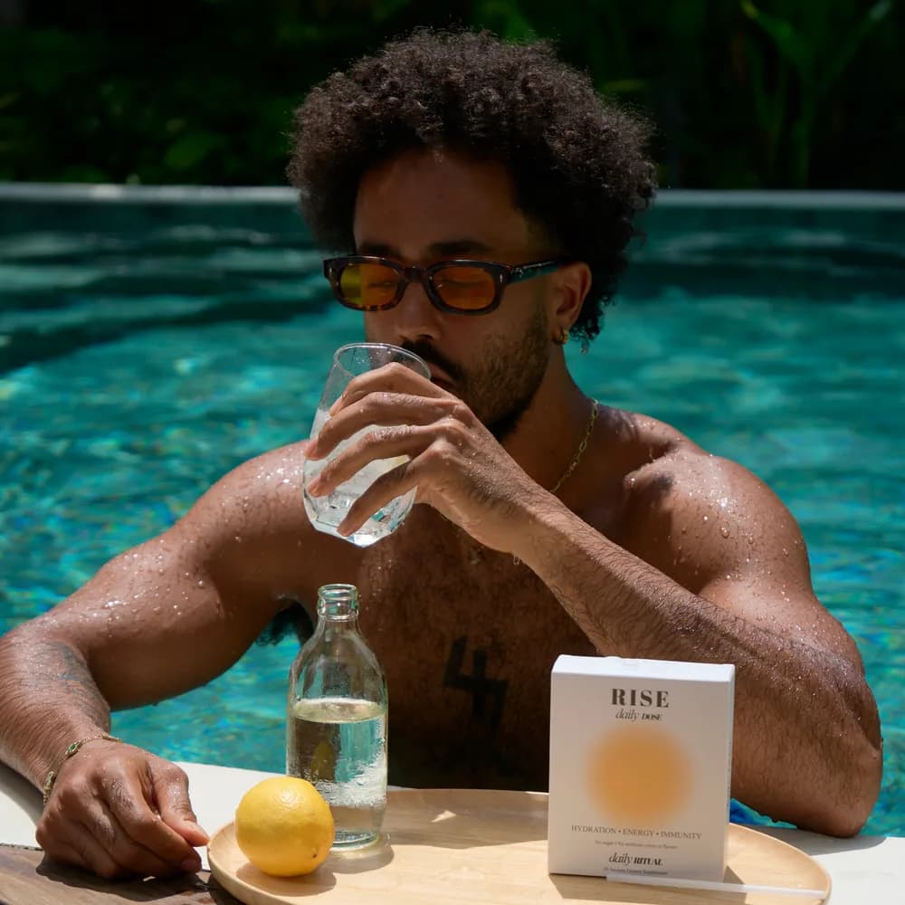 A man by the pool drinking a glass of RISE Daily Dose